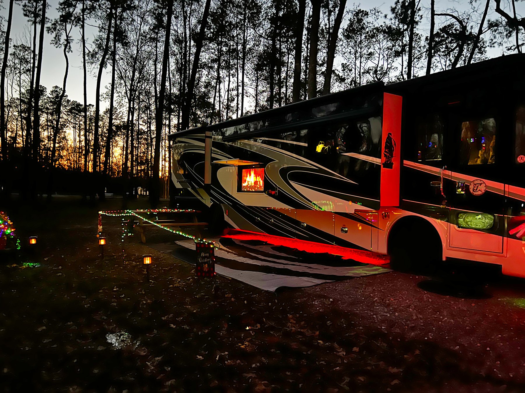Large Class A motorhome parked at a wooded RV site at twilight in winter