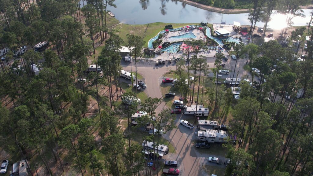 Aerial view of a Louisiana campground with RV sites among pines, pools, a lazy river, and a lake