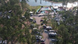 Aerial view of a Louisiana campground with RV sites among pines, pools, a lazy river, and a lake