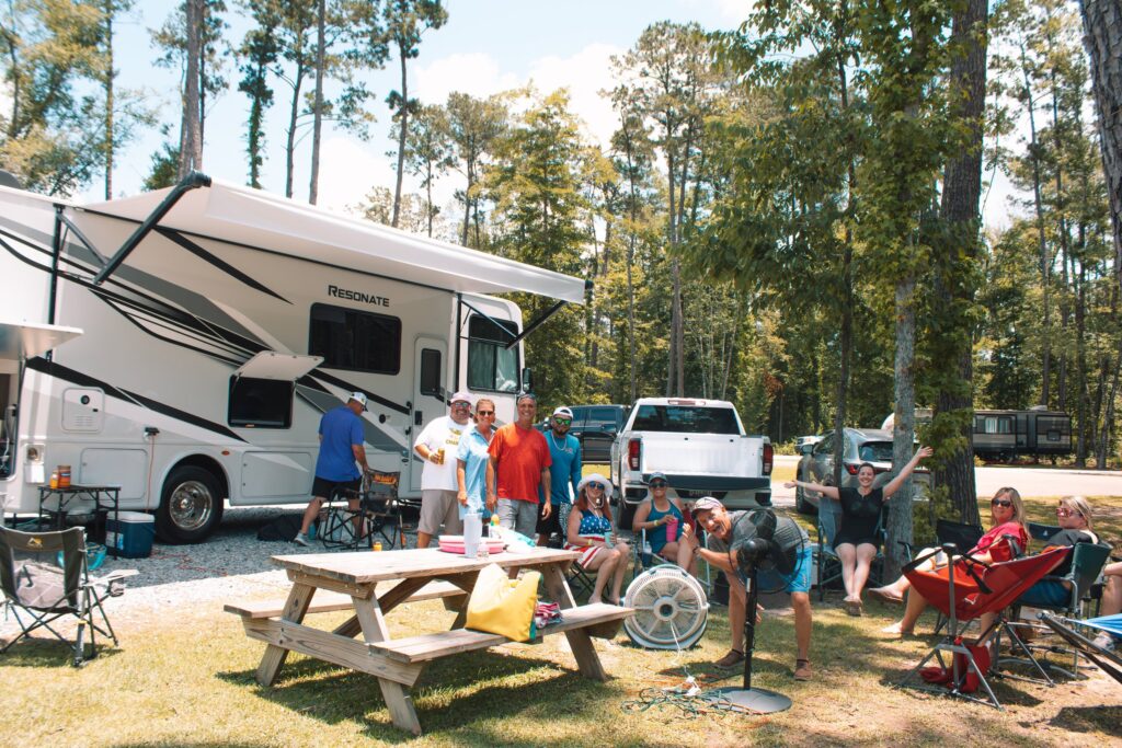 Family and friends gathered at a shaded RV site under tall pines at Fireside RV Resort in summer