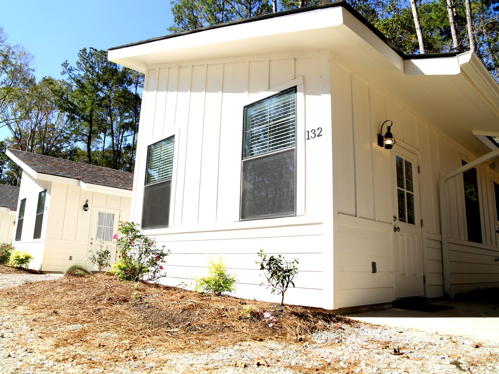 White board-and-batten rental cabin among tall pine trees at Fireside RV Resort in Ponchatoula