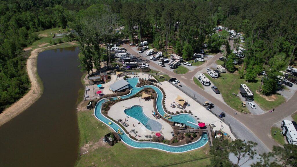 Aerial view of Fireside RV Resort near New Orleans showing the lazy river, pools, lake, and RV sites among pine trees in summer